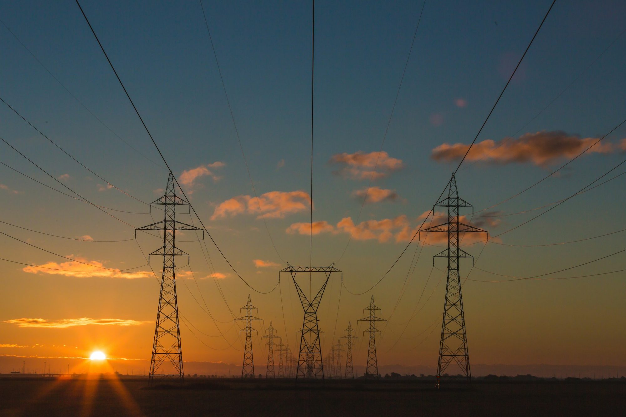 Torres de transmissão de energia elétrica ao pôr do sol, representando a infraestrutura do setor elétrico e a gestão de ETR.